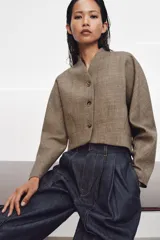 Chaqueta corta de corte estructurado confeccionada en tejido con mezcla de lana. Presenta cuello en pico, cierre frontal con botones y mangas largas. El diseño incluye bolsillos delanteros y un forro interior a contraste.