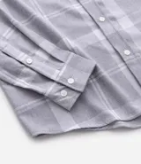 Camisa de franela de manga larga con estampado de cuadros en blanco y negro. Presenta cuello inglés, cierre frontal con botones y bolsillo en el pecho.