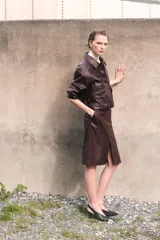 Pollera tubo de cuero sintético color marrón oscuro, de largo hasta la rodilla, con tajo frontal y cierre oculto en la parte trasera.