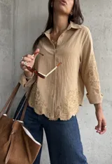 Camisa de lino color camel con cuello clásico, cierre frontal de botones y mangas largas. Presenta un delicado bordado floral tono sobre tono en las mangas y en el ruedo, el cual tiene un acabado festoneado.