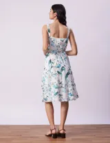 Vestido midi blanco con estampado floral celeste y verde, escote recto con tirantes, abertura frontal con botones, lazo en la cintura y bolsillos laterales.