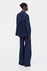 Campera camisera de denim azul oscuro con cuello, cierre frontal de botones, hombros caídos, mangas largas con puños abotonados y dos bolsillos delanteros de parche.