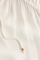 Blusa oversized de viscosa color beige con escote en V pronunciado, cordones ajustables con cuentas en los extremos, hombros caídos y mangas globo largas con puños elásticos.