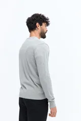 Sweater de punto color gris melange, con escote en V, manga larga y logo bordado en el pecho. Presenta puños y ruedo acanalados.
