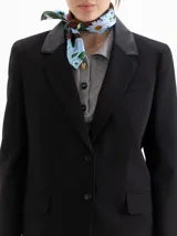 Blazer negro de corte sastrero con solapas en cuero vacuno. Presenta cierre frontal con broches forrados, bolsillos laterales con tapa y bolsillo relojero. Cuenta con tajos en la espalda y un largo que sobrepasa la cadera.