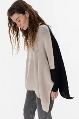 Poncho de tejido de punto con diseño oversize y aberturas laterales. Presenta un acabado con destellos brillantes y cuello redondo amplio.