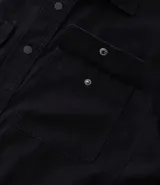 Camisa de manga larga confeccionada en sarga de algodón color verde menta, con cuello inglés y cierre frontal de botones negros. Presenta dos bolsillos de parche con solapa en el pecho y puños con botones.