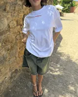 Remera blanca de algodón con corte oversize y estampado grande en la espalda de dos cerezas rojas unidas por el tallo, con el texto "Nude® Project" debajo.