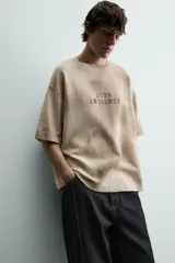 Camiseta de punto de algodón con corte relajado (relaxed fit) y cuello redondo. Presenta un estampado frontal con efecto spray en tonos marrones y beige, y un efecto lavado general.