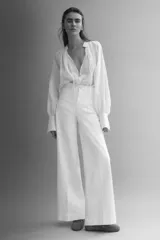 Jean de denim de algodón blanco con leve elasticidad, tiro alto y diseño de pierna ancha (wide leg). Cuenta con bolsillos de parche delanteros, botón metálico con diseño y pliegues marcados al frente y en la espalda.