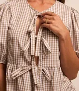 Blusa de tricolina de algodón con estampado de cuadros vichy, mangas cortas abullonadas, cuello redondo, abertura delantera con lazos y recorte fruncido en la cintura.