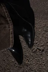 Botín estilo cowboy de caña baja, confeccionado en material sintético con acabado liso. Presenta un diseño de punta fina, tacón curvo en bloque y cierre mediante cremallera lateral.