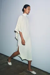 Vestido midi fluido de cuello alto y manga corta tipo capa. Presenta un diseño minimalista con bajo recto y aberturas laterales, con cierre en la espalda.