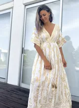 Túnica larga de estilo bohemio, color blanco con estampado de arabescos en tono dorado. Presenta escote en V profundo, mangas amplias tipo kimono y ajuste elástico en la cintura con cordón decorativo terminado en borla.
