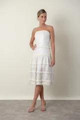Vestido midi strapless color marfil, con diseño de paneles horizontales que combinan encaje y detalles de flecos. Presenta una falda con vuelo y movimiento.