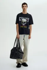Remera negra de algodón de peso medio, corte holgado (Loose Fit), con cuello redondo. Estampado frontal con el logo de Guns N' Roses, una calavera con una rosa y una cadena, y el texto "Appetite for Destruction 1987-1988".