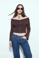 Top de punto acanalado negro, con diseño off-shoulder y escote amplio. Presenta mangas largas y cierre frontal completo con doble cursor, permitiendo ajustar la apertura superior e inferior.