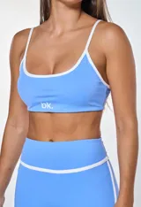 Conjunto deportivo compuesto por un top y un short de color celeste con detalles en blanco. El top tiene breteles finos y el logo 'bk.' estampado en el frente. El short es de tiro alto con una banda blanca horizontal en la cintura y líneas laterales blancas.