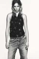 Top halter de tul color gris claro, con escote fluido drapeado y espalda descubierta. Presenta bordados con aplicación de abalorios en tonos oscuros y dorados.