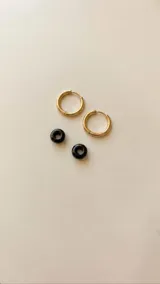 Aros de acero quirúrgico dorados en forma de argolla con dijes de piedra natural negra en forma de dona, desmontables.