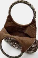 Bolso de mano mini con cuerpo de efecto aterciopelado en color marrón, adornado con abalorios y lentejuelas que forman un estampado floral. Cuenta con doble asa de mano rígida decorada con cuentas y cierre magnético.