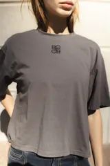 Remera blanca de algodón con corte boxy y cuello redondo. Presenta un pequeño logo bordado en color cobre en el centro del pecho.