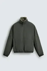 Cazadora de corte relajado confeccionada en tejido técnico color verde oscuro, con interior de borreguillo, cuello subido, cierre frontal de cremallera y bolsillos laterales con cremallera.