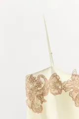 Top de tejido satinado color beige, con escote recto y tirantes finos ajustables. Presenta un detalle de aplicación de encaje bordado a contraste en la parte superior.