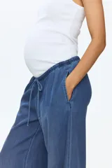 Pantalón de denim suave color azul, de corte holgado estilo globo con piernas abombadas, cintura elastizada con cordón ajustable y bajos con elástico y cintas para ajustar.