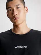 Conjunto de pijama Calvin Klein compuesto por una remera negra de cuello redondo con logo estampado en el pecho y un short verde con estampado tipográfico de la marca.