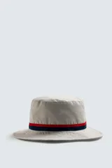 Sombrero tipo bucket de algodón color beige claro, con cinta decorativa a rayas rojas y azul marino alrededor de la copa.