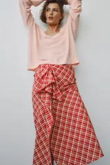 Falda midi de tiro medio ZARA WOMAN COLLECTION confeccionada en hilatura con algodón, con estampado de cuadros en tonos rojos y blancos. Presenta detalle de pliegue con lazadas en el delantero y bajo recto con abertura. Cierre con cremallera oculta en costura.