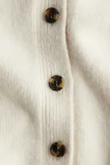 Saco de punto suave con cuello camisero, cierre frontal con botones y mangas cortas. Presenta terminaciones acanaladas en mangas y ruedo.