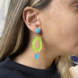 Par de aros colgantes con pasador de acero quirúrgico. Presentan un círculo celeste con un strass, un óvalo calado amarillo y una gota celeste.