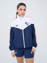 Campera deportiva Umbro del Club Nacional de Football, modelo Sky para mujer. Diseño con cierre frontal, cuello alto y bloques de color en blanco, azul marino y detalles en rojo. Incluye el logo de Umbro y el escudo del club.