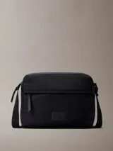 Bolso bandolera Calvin Klein color negro, confeccionado en nylon reciclado, con cierre de cremallera, asa superior y correa ajustable. Presenta un bolsillo frontal con cremallera y parche con el monograma CK en la parte delantera.