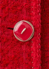 Chaqueta corta roja de tejido texturizado tipo tweed, con cuello redondo, bolsillos frontales con solapa, mangas largas y cierre de botonadura frontal con botones decorativos.
