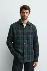 Camisa de corte regular fit confeccionada en tejido doble de algodón, con diseño de cuadros en tonos verde y azul marino. Presenta cuello solapa, manga larga con puño abotonado, bolsillo plastrón en el pecho y cierre frontal con botones.