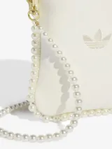 Mini bolso tipo bandolera de color blanco, con diseño minimalista y logo de Adidas bordado en el frente. Presenta un borde decorado con perlas sintéticas que se extienden hacia la correa, aportando un toque elegante y distintivo.