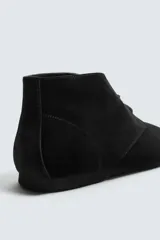 Bota tipo derby de caña baja, confeccionada en piel con acabado de serraje en color negro. Presenta cierre de cordones, horma redonda y suela de goma Vibram.