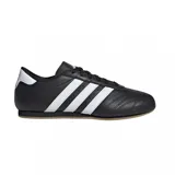 Championes Adidas modelo Taekwondo Lace, de diseño minimalista en color negro con las tres tiras características en blanco y detalle en el talón. Presentan una silueta de perfil bajo con costuras reforzadas en la puntera y suela de goma color caramelo.