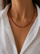 Collar de cuentas pequeñas color rojo con detalles intercalados de esferas doradas. Cuenta con una cadena de extensión terminada en un dije pequeño en forma de corazón.