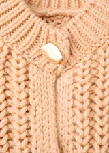 Cardigan de punto grueso color beige, de cuello redondo, manga larga y diseño recto. Presenta cierre frontal con botones efecto joya.
