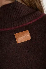 Polera de punto con calce oversize, cuello alto y mangas largas. Presenta un diseño en color negro con franjas laterales en las mangas y detalle en el cuello en tono bronce con acabado brillante.