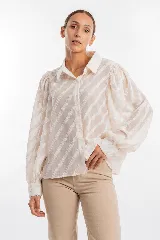 Camisa de manga larga color blanco marfil con patrón de rayas diagonales semitransparentes, cuello camisero, cierre frontal con botones y mangas abullonadas con puños ajustados.