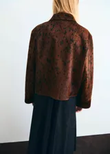 Chaqueta de cuero de potro color marrón con estampado tipo animal print en tonos oscuros, de corte recto y largo recortado. Cuenta con cuello camisero, cierre frontal de cremallera metálica y mangas largas amplias con puños rectos.