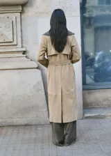 Gabardina larga de piel caprina en color beige, con solapas amplias, cierre cruzado con botones y cinturón ajustable del mismo material.