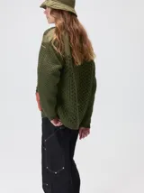Campera tejido grueso y abrigado color verde militar, con forro de nylon interno, cuello estilo camisa en color negro y cierre frontal con botones. Cuenta con cuatro bolsillos delanteros con apliques en distintos tonos y texturas, y un parche bordado circular en el bolsillo superior izquierdo.