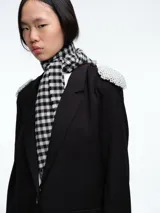 Blazer negro de corte estructurado con hombreras decoradas con apliques de perlas. Presenta cierre frontal con un botón, solapas clásicas y bolsillos laterales con solapa.