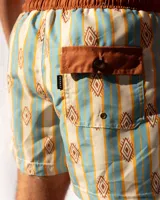 Short de baño de microfibra con estampado de rayas verticales en tonos celeste y beige, con motivos geométricos en color ocre. Tiene cintura elastizada marrón con cordón ajustable, dos bolsillos laterales y uno trasero.